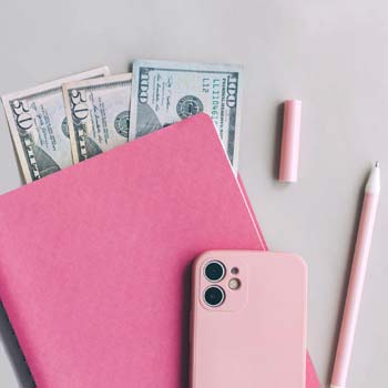 Pink iPhone and pencil sitting atop pink folder containing cash money